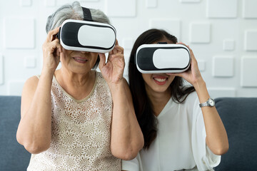 Older mature mother and young grownup daughter getting experience playing VR-headset glasses of virtual reality at home.