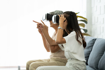 Older mature mother and young grownup daughter getting experience playing VR-headset glasses of virtual reality at home.
