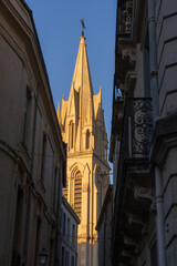 Vertical view of the bell tower of St Anne ancient catholic church through narrow street catching early morning sunlight, Montpellier, France
