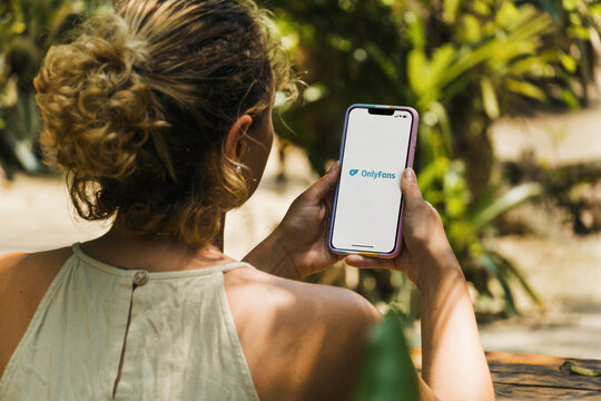 Girl in the park holding a smartphone with OnlyFans app on the screen. Rustic wooden table. Rio de Janeiro, RJ, Brazil. July 2022