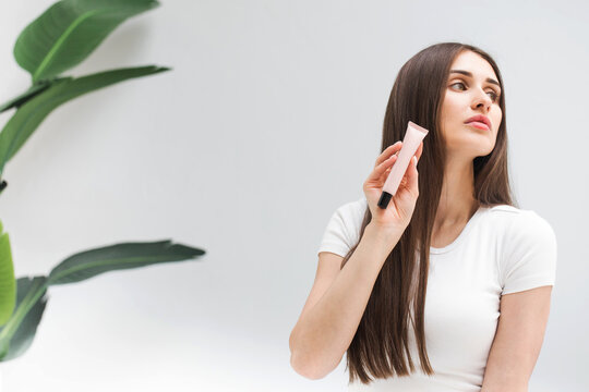 Woman with straight hair shows small tube of cosmetic product in studio closeup