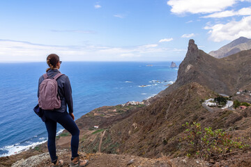 Backpack woman with scenic view of Atlantic Ocean coastline and Anaga mountain range on Tenerife, Canary Islands, Spain, Europe. Looking at Roque de las Animas crag. Hiking trail from Afur to Taganana