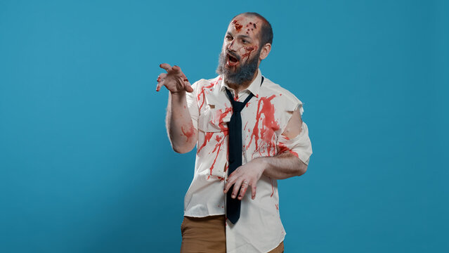 Goofy Ugly Zombie Dancing Childish On Blue Background. Creepy Mindless Brain-eating Monster With Deep And Bloody Wounds And Scars Enjoying Dance While Looking At Camera. Studio Shot