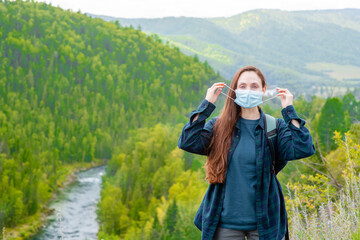 Young woman put on face mask during coronavirus and flu outbreak stands in mountains
