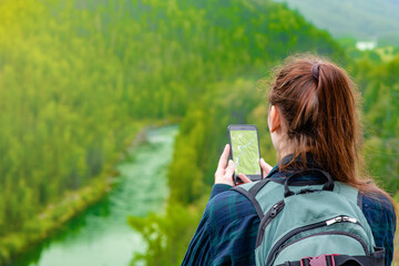 Young woman uses smartphone at mountains and using travel app or map during her hike. Empty space...