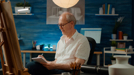 Male artist taking notes on textbook and sketching vase model to draw professional artwork design. Drawing modern art sketch with inspiration, using notebook and artistic skills.