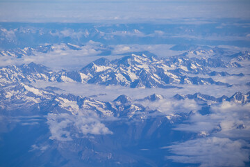 Window view from an airplane on the snow capped mountain ranges of the Alps at the border Austria Italy, Europe, EU. High peak are shrouded in clouds. Flying high above the ground. Freedom