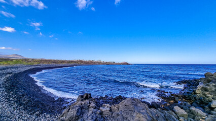 Scenic view on black stone pebble beach Playa Colmenares near Amarilla, Golf del Sur, Tenerife, Canary Islands, Spain, Europe. Vacation resort complex. Waves from Atlantic Ocean. Montana Roja in back