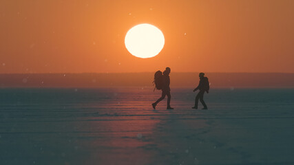 The romantic couple walking through the snow field on sunset background