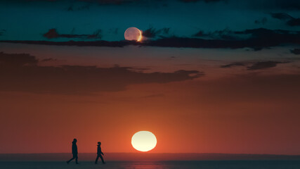 The two tourists walking through the snow field on beautiful sunset background