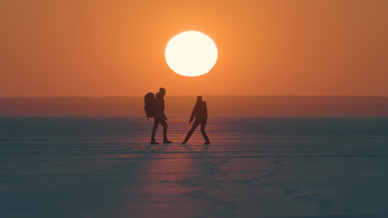 Fototapeta na wymiar The two travelers walking through the arctic snowy field on sunset background