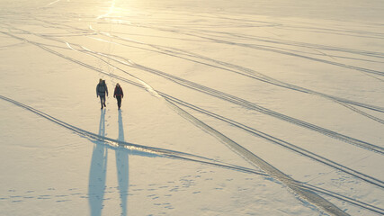 The aerial view on two travelers walking through the snow field