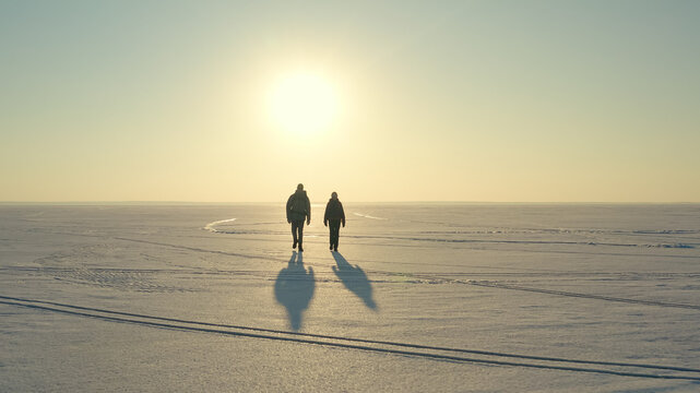 The couple of travelers walking through the snow field on sunset background
