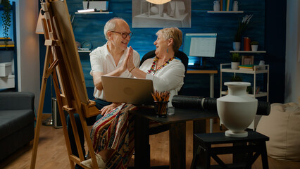 Old man and woman doing teamwork to draw vase artwork, using laptop computer to find modern inspiration online. Team of artists drawing with artistic tools and creative skills, sketch masterpiece.