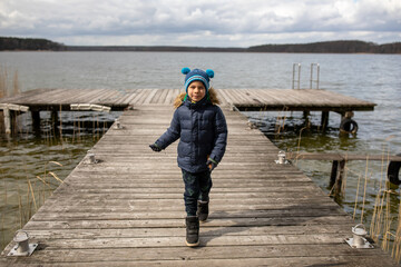 Little boy running on pier against lake on sunny autumn cool day outdoors