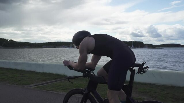 Triathlete rides a cutting bike, pro cyclist rides on a road near a lake, an athlete trains before a triathlon competition.