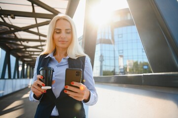 Fototapeta premium Business Woman With Phone Near Office. Portrait Of Beautiful Smiling Female In Fashion Office Clothes Talking On Phone While Standing Outdoors. Phone Communication. High Quality Image.