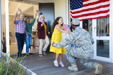 Excited multiracial multigeneration family with flag of america welcoming army soldier in house