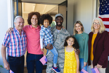 Portrait of smiling multiracial soldier with multigeneration family standing at entrance of house