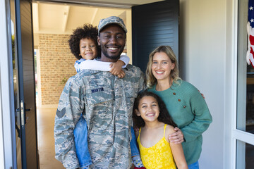 Portrait of happy multiracial soldier with woman and children standing at entrance of house
