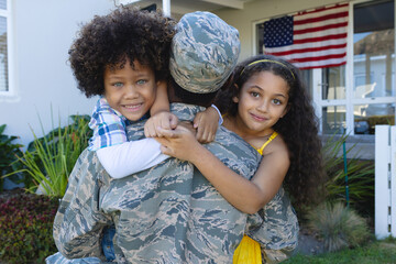 Portrait of excited multiracial boy and girl embracing military father returned home