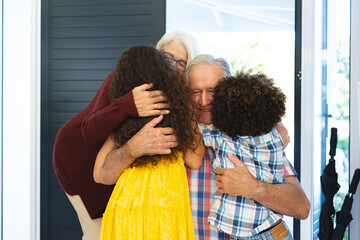 Multiracial grandchildren embracing grandparents while welcoming them at home at entrance