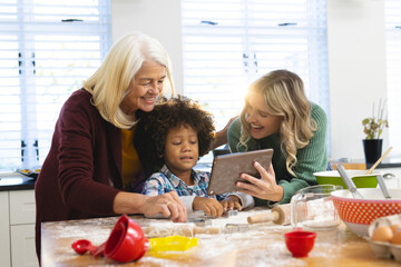 Cheerful multiracial mother and grandmother showing recipe to boy over digital pc in kitchen