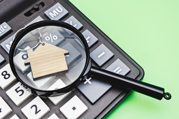 The concept of mortgage, sale and rental of housing and real estate. Mortgage credit lending. Calculator with a wooden house under a magnifying glass on a blue background. Copy space.