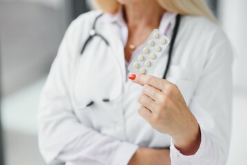 Smiling middle aged female therapist in white uniform holds pills.