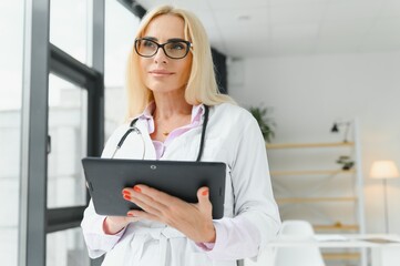 Portrait of beautiful mature woman doctor holding digital tablet. Confident female doctor using...