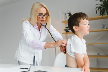Obraz premium Doctor pediatrician examines child. Female doctor puts a stethoscope to a child's chest and listens to the little boy's heartbeat and lungs. Concept of health care and pediatric medical examination.