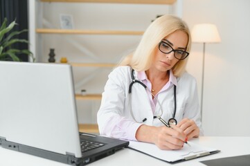 Portrait shot of middle aged female doctor sitting at desk and working in doctor office