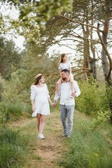 Fototapeta premium Happy family. Dad, pregnant mom and little daughter play games at sunset in summer in park.