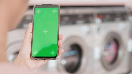 Woman using digital smart phone on laundry during waiting washing machine working, self-service laundry facility, female setting application for washing on smartphone green screen - Powered by Adobe
