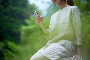 自然の中でスマートフォンを持つ若い日本人女性