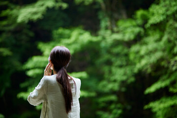 自然の中でワイヤレスイヤホンで音楽を聴く若い日本人女性