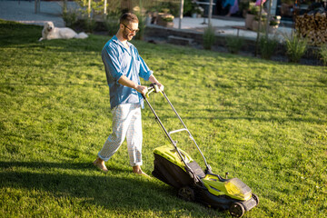 Man mows the lawn with lawn mower at backyard of his house. Husband takes care of garden on summer...