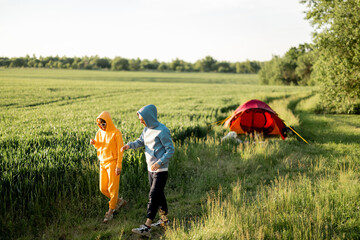 Young couple have fun, walk and talk together while traveling with tent on green field during summer time