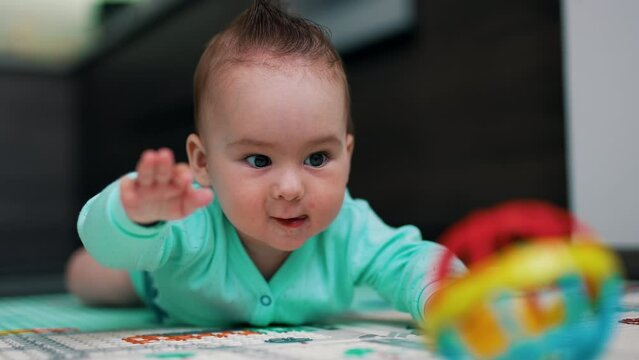 Adorable infant baby with funny hairdo claps his hands by the floor. Child looks curiously at toy showing tongue.