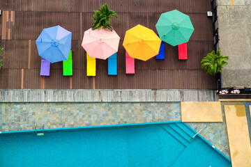 Aerial view of pool, swimming people in transparent blue water, umbrellas, sunbeds, green trees at...