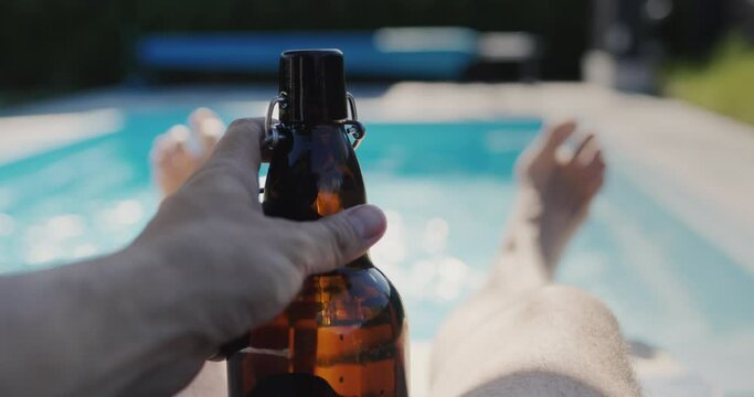 A man with a bottle of beer is relaxing near his pool on a hot summer day