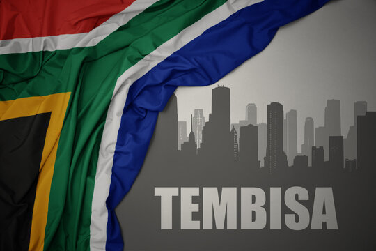 abstract silhouette of the city with text Tembisa near waving colorful national flag of south africa on a gray background.