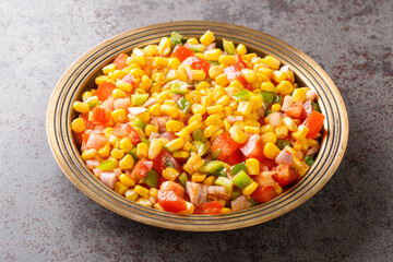 Corn chaat is a super quick snack made with boiled corn, chaat masala, spice powder, onions and tomatoes on a plate closeup on the table. Horizontal