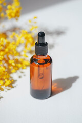 Amber dropper bottles with serum, tonic or essential oil with yellow flowers. White background with...