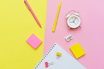 White notepad on spring and stationery school supplies on a pink background, heaps of colored pencils, paper clips, multi-colored objects for work and creativity, back to school