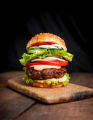 Burger with beef meat, cheese, lettuce, onion, tomato, cucumber, mayo and ketchup on an old wooden table. Junk food concept