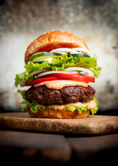 Burger with beef meat, cheese, lettuce, onion, tomato, cucumber, mayo and ketchup on an old wooden table. Junk food concept