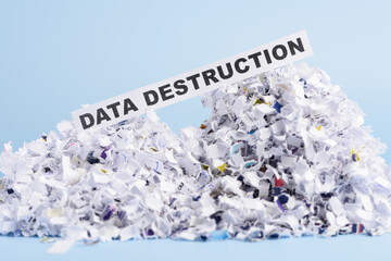 Words Data destruction on top of heap of cross shredded paper concept on blue background