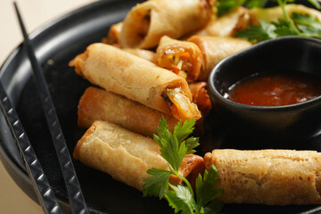Traditional southeast asian starter dish spring or summer rolls - deep fried dim sum dumplings stuffed with vegetables with sweet-sour sauce and fresh coriander on black plate with black chop sticks