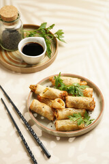 Traditional southeast asian starter dish spring or summer rolls - deep fried dim sum dumplings stuffed with vegetables with soy sauce, fresh coriander on grey plate with black chop sticks